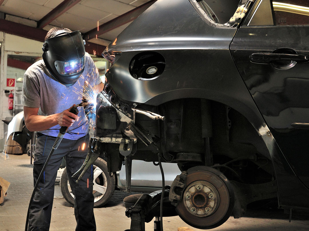 Technician welding and repairing a car body panel in the shop